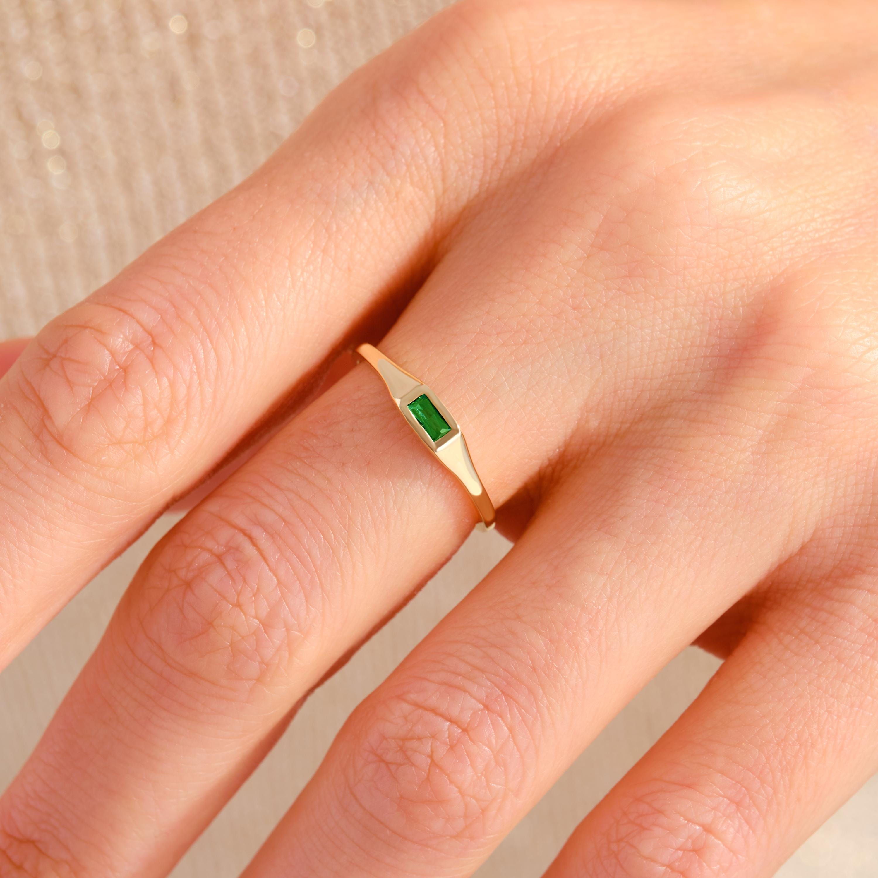 May include: A gold ring with a small, rectangular, emerald green gemstone set in the center.