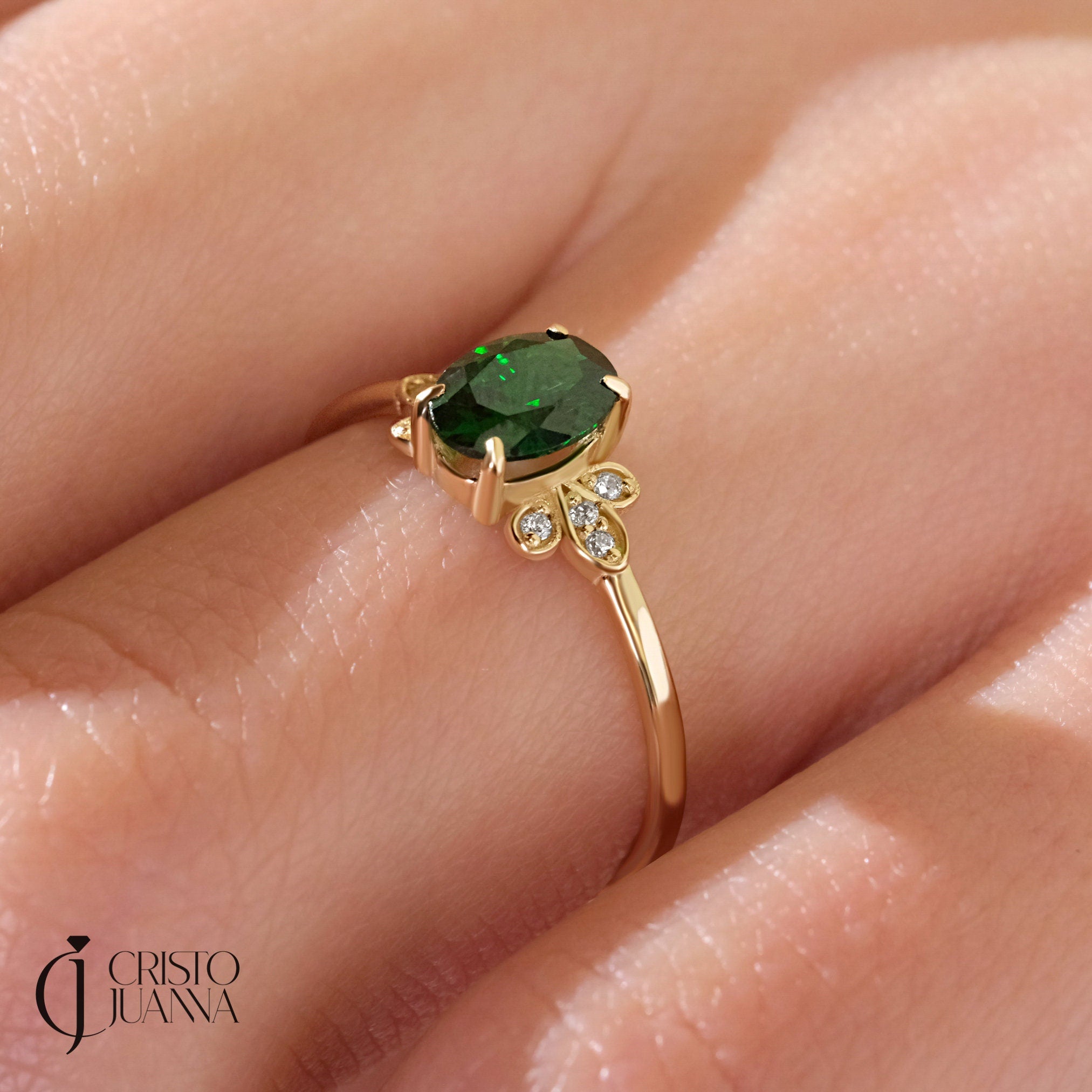 Close-up of a 14K gold oval emerald engagement ring with a thin moissanite band. A perfect emerald moissanite ring for her, crafted with delicate detail.