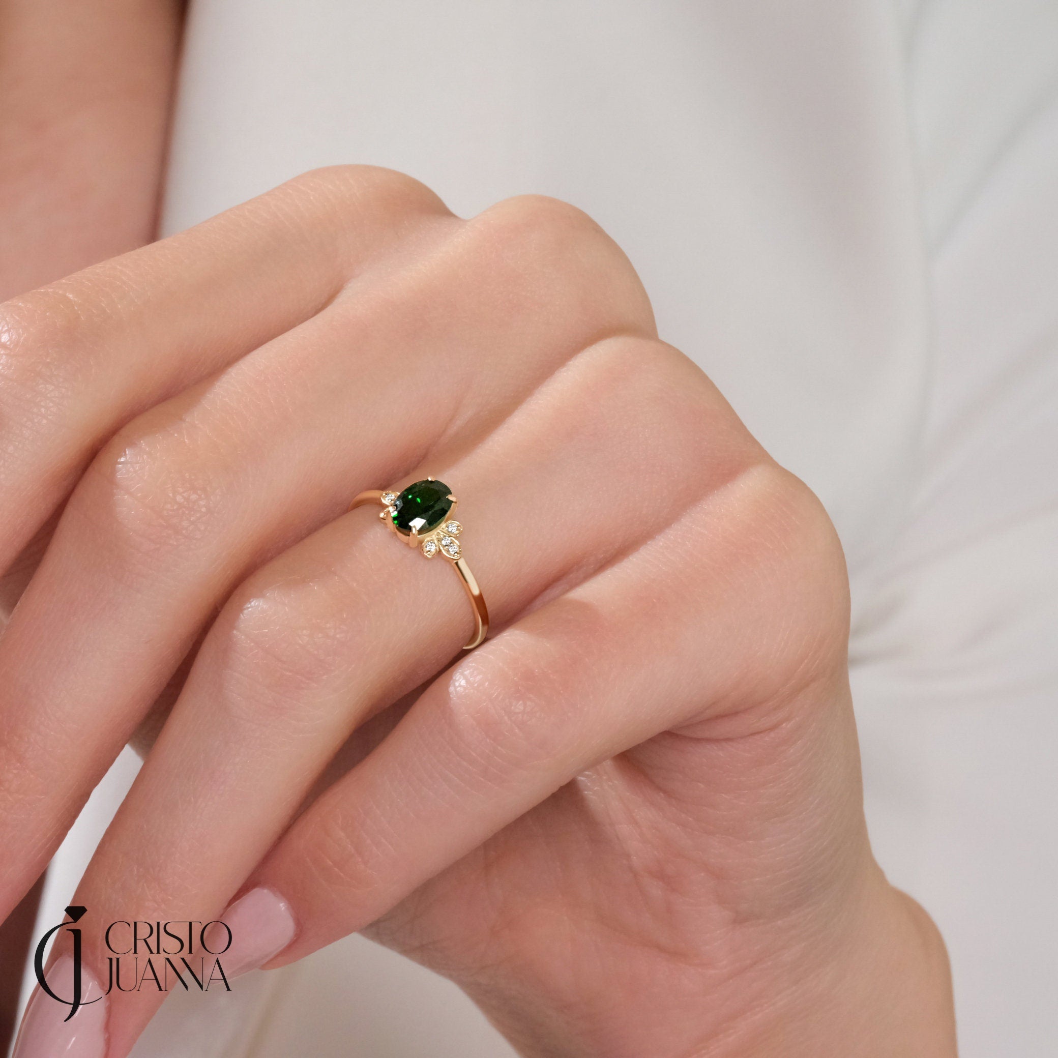 14K gold oval emerald engagement ring worn on a finger, showcasing its elegant design with a thin moissanite band, ideal for special occasions or daily wear.